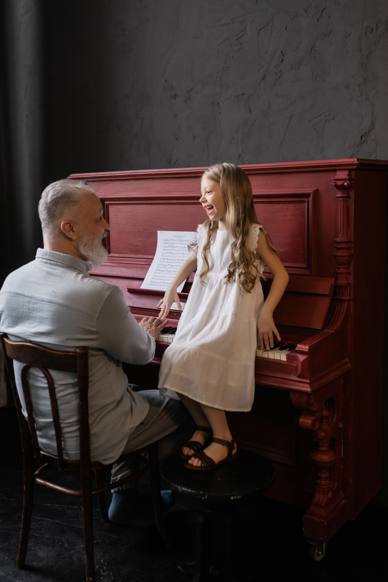 Un grand-père et sa petite-fille rient ensemble près d’un piano.